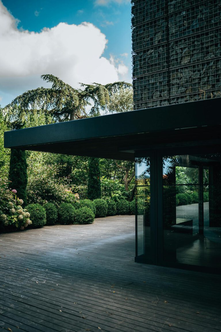 Contemporary building facade surrounded by lush garden and wooden deck.